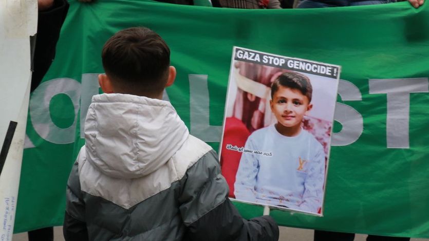Boy in France holds signs that reads "Gaza Stop Genocide!"