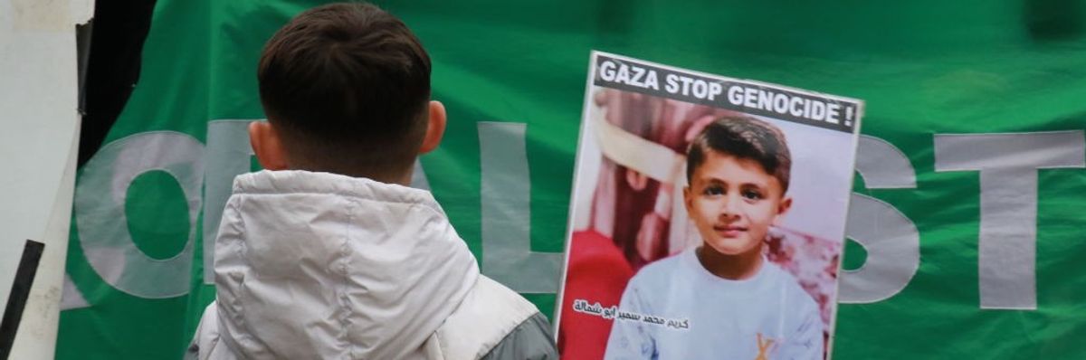 Boy in France holds signs that reads "Gaza Stop Genocide!"