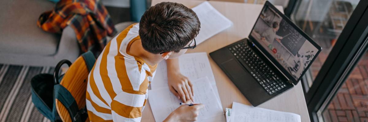 Boy participating in online education training class with teacher using laptop at home