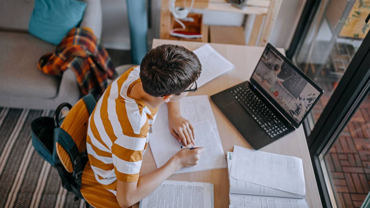 Boy participating in online education training class with teacher using laptop at home