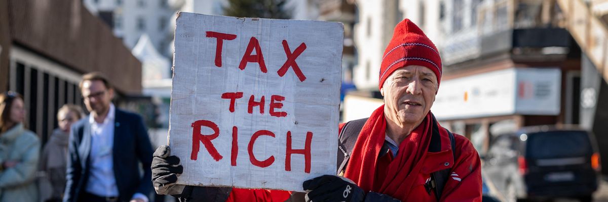 British millionaire, poses with a placard reading "Tax the rich"