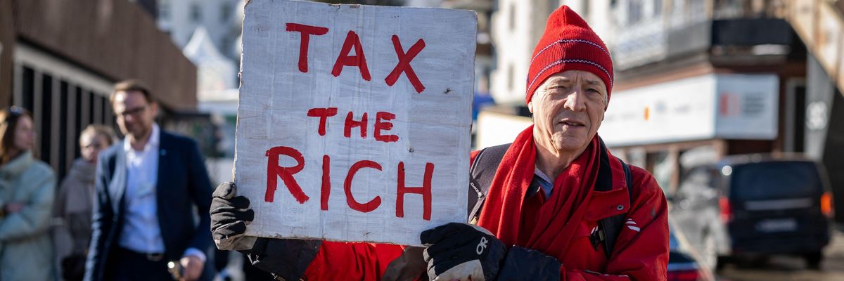 British millionaire, poses with a placard reading "Tax the rich"