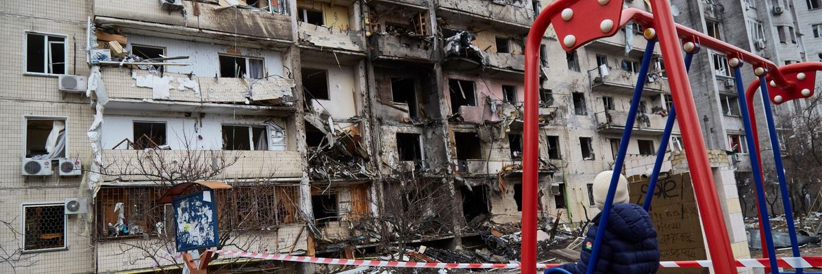 child on swing in front of destroyed building