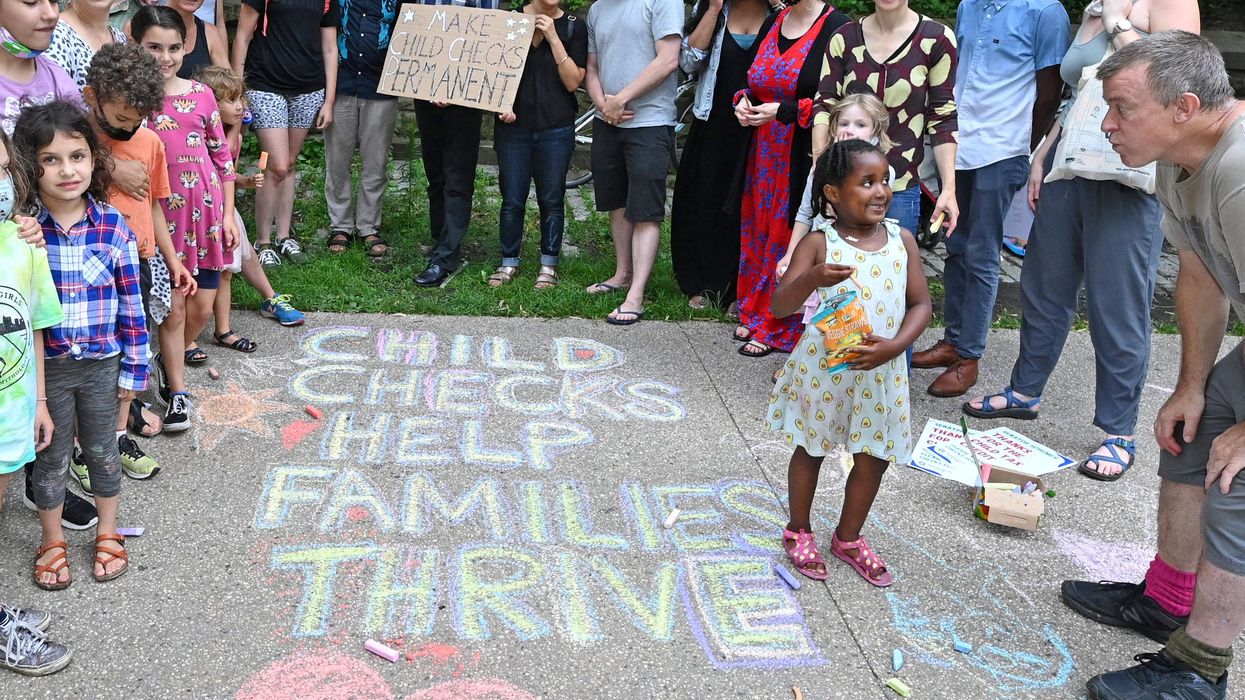 Children and parents stand next to a message in sidewalk chalk reading, "Child checks help families thrive."