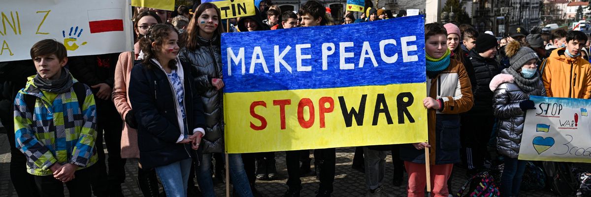 Children hold a yellow and blue sign saying, "Make peace, stop war."