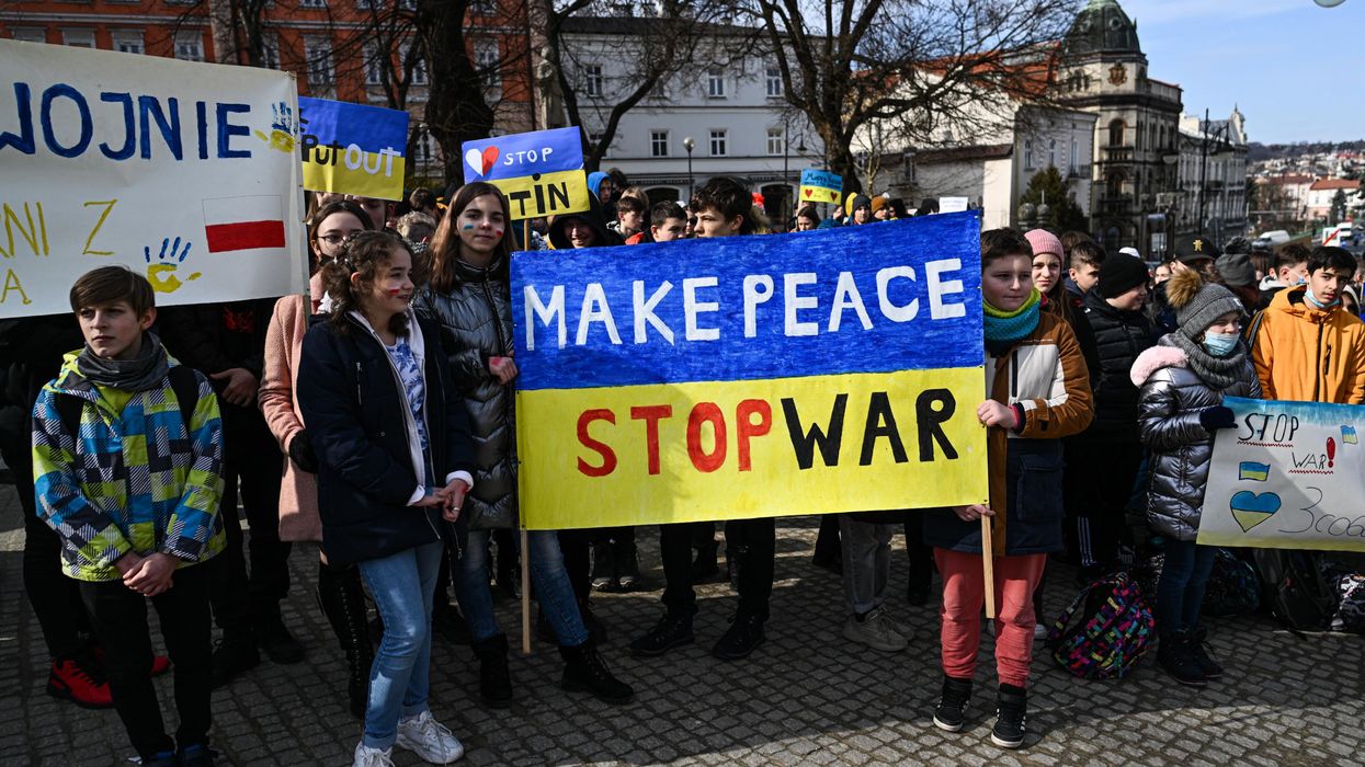 Children hold a yellow and blue sign saying, "Make peace, stop war."