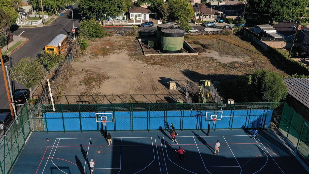 Children play basketball beside an oil well pump jack and tank,