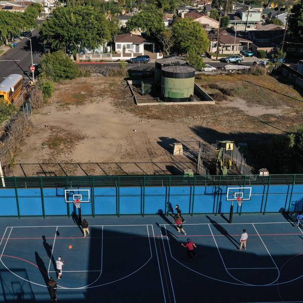 Children play basketball beside an oil well pump jack and tank,