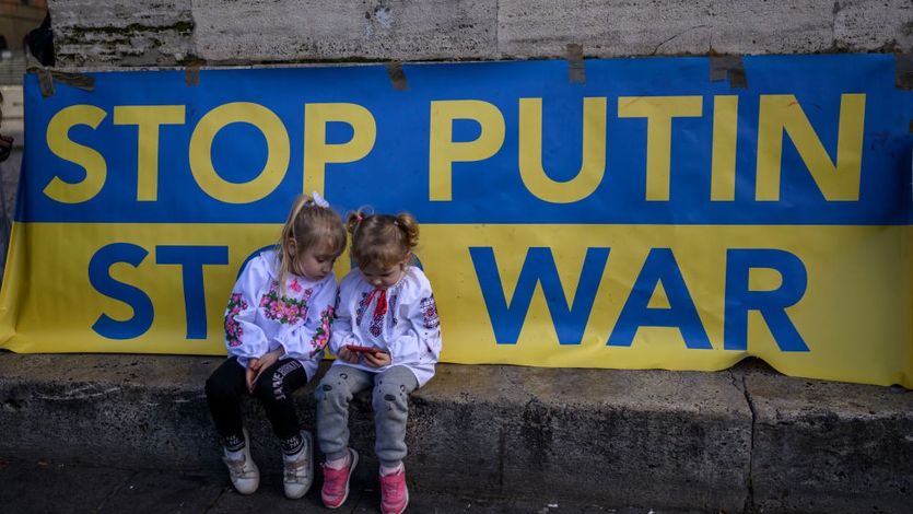 Children sit in front of a sign that says "Stop Putin, Stop War"