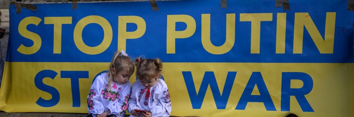 Children sit in front of a sign that says "Stop Putin, Stop War"