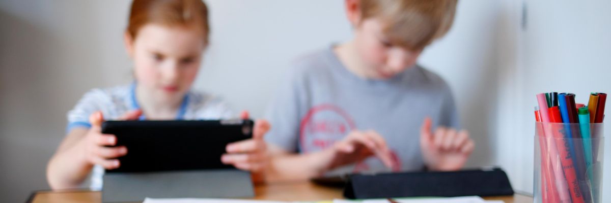 Children use computer tablets at a desk. 