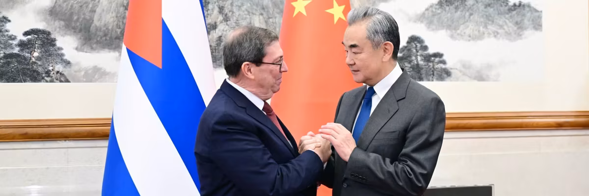 Chinese and Cuban foreign ministers shake hands standing next to the two countries' flags