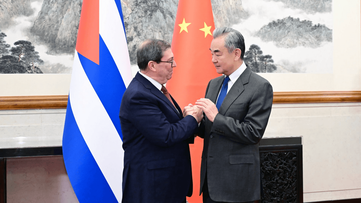 Chinese and Cuban foreign ministers shake hands standing next to the two countries' flags