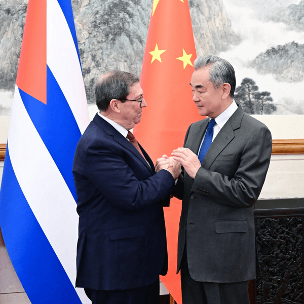 Chinese and Cuban foreign ministers shake hands standing next to the two countries' flags