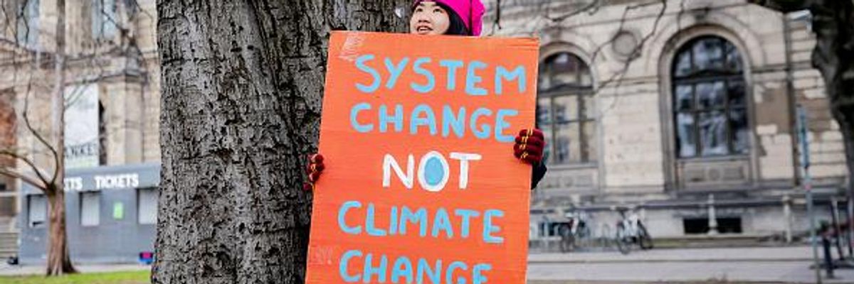 Climate activist Howey Ou holds a sign reading, "System Change Not Climate Change" 