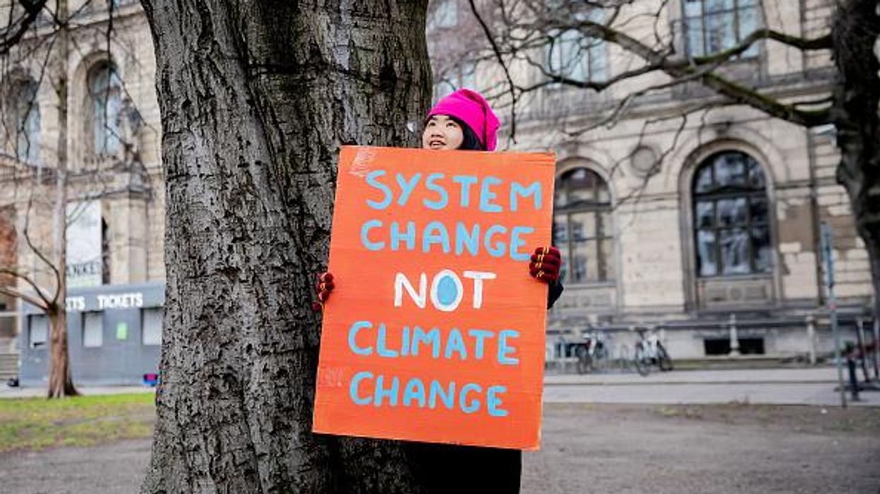 Climate activist Howey Ou holds a sign reading, "System Change Not Climate Change"