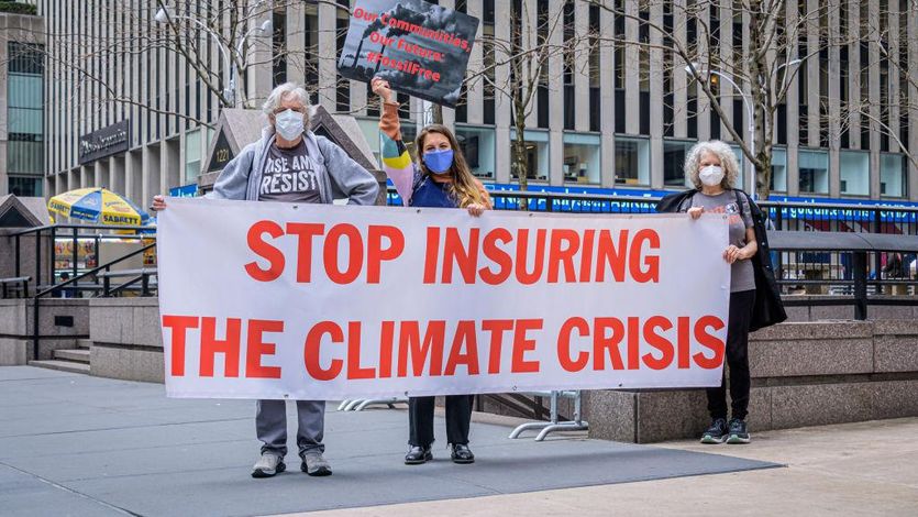 Climate activists hold a sign saying, "Stop insuring the climate crisis."