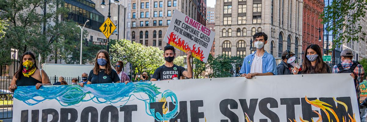 Climate activists holding sign that reads "Uproot the system"