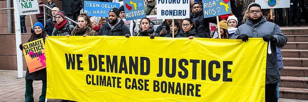 Climate activists stand with a banner saying, "We demand justice. Climate case Bonaire."