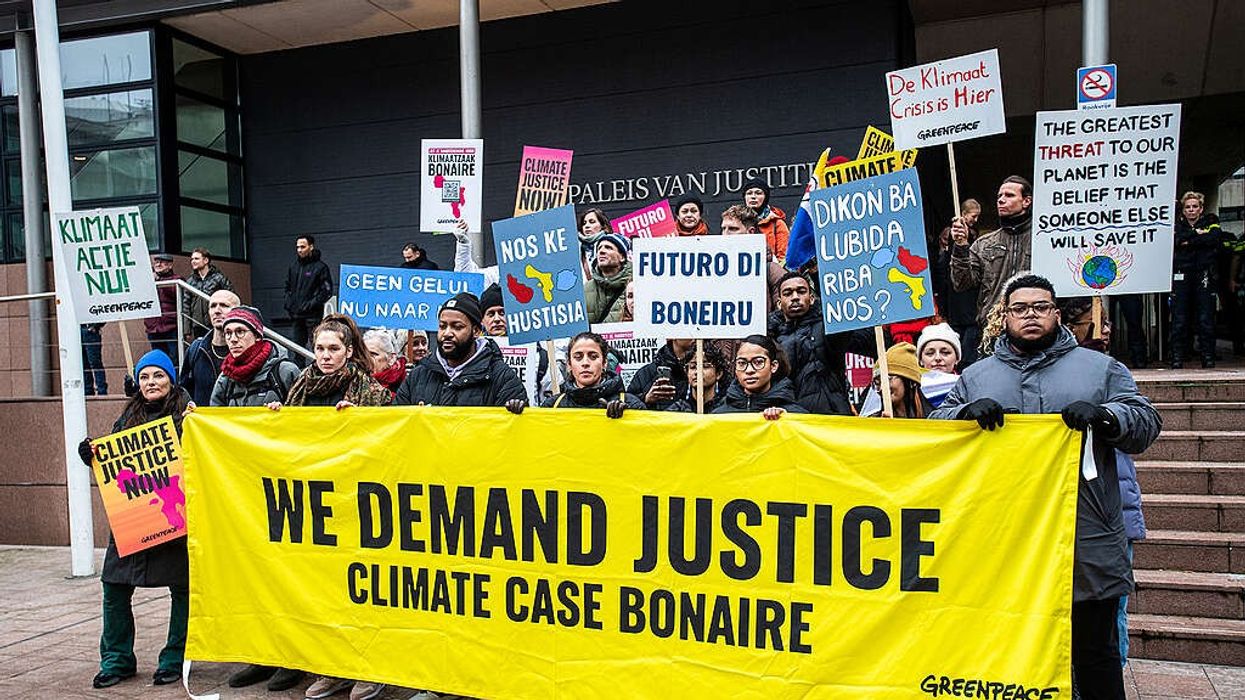 Climate activists stand with a banner saying, "We demand justice. Climate case Bonaire."