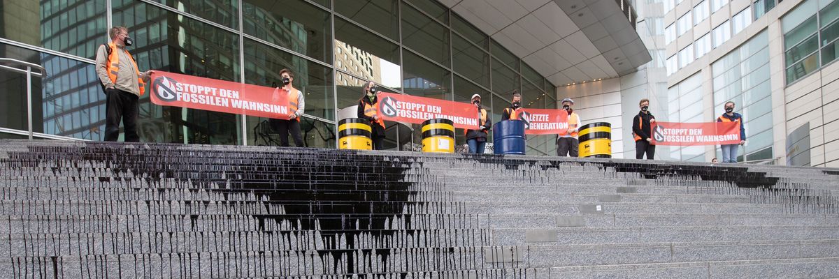 Climate activists standing on steps of Commerzbank in Germany with oil-like liquid dripping down the steps.