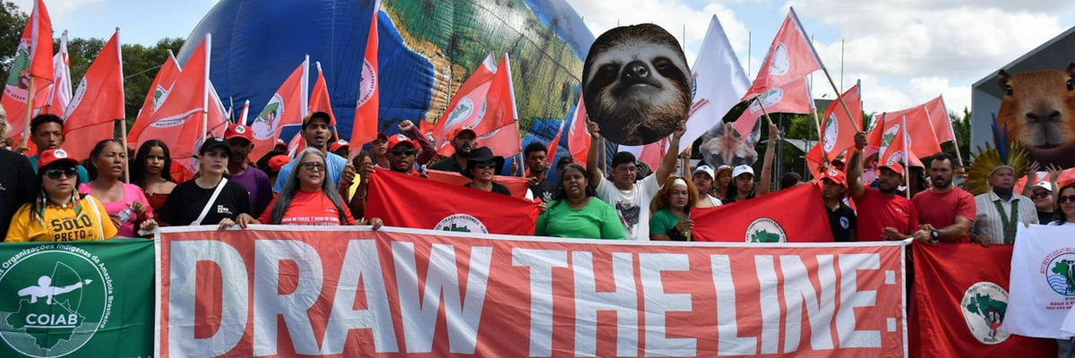 Climate defenders march with a banner reading, "Draw the Line: COP30 Must Be the Turning Point"