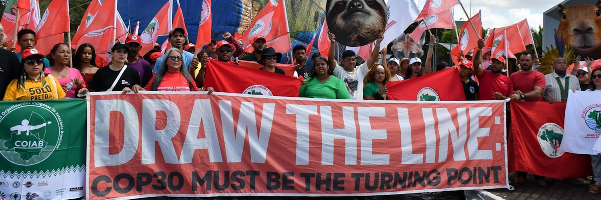 Climate defenders march with a banner reading, "Draw the Line: COP30 Must Be the Turning Point"