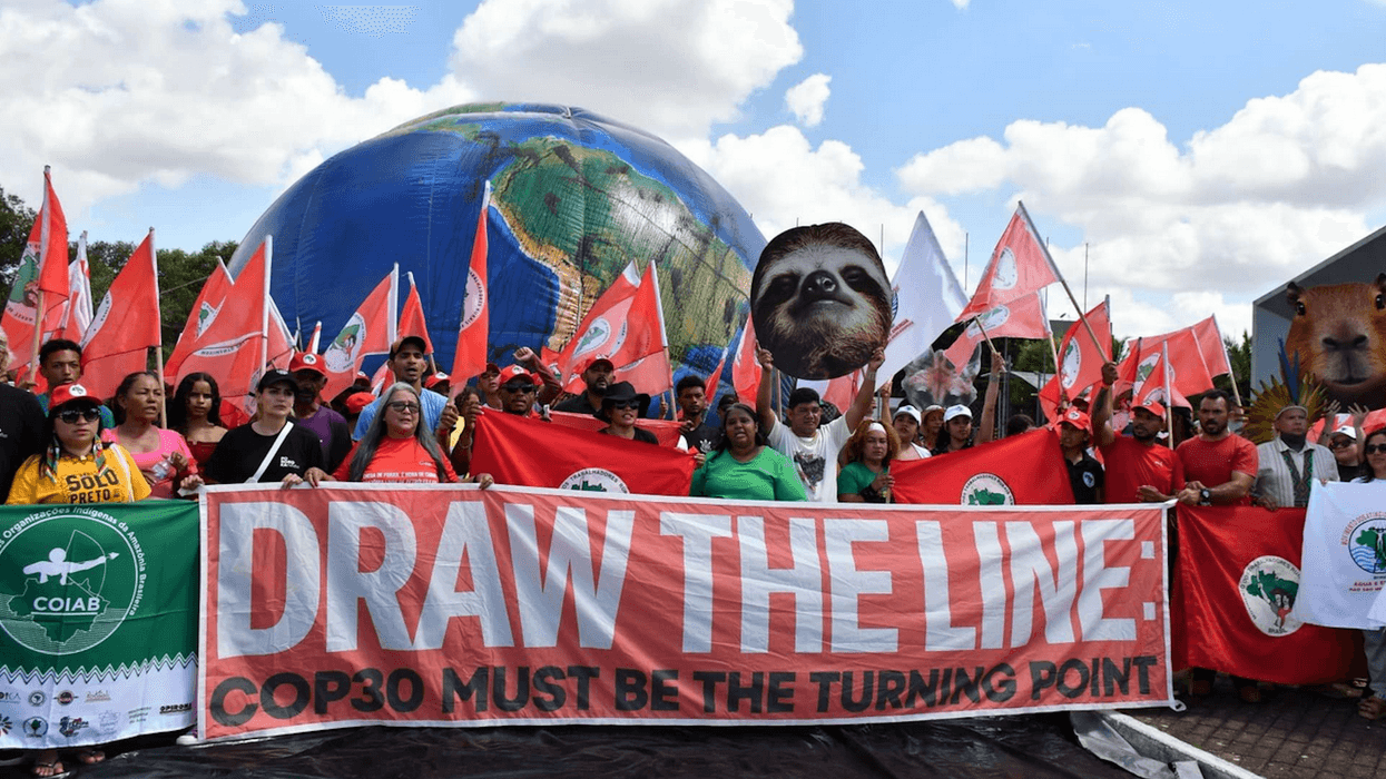 Climate defenders march with a banner reading, "Draw the Line: COP30 Must Be the Turning Point"