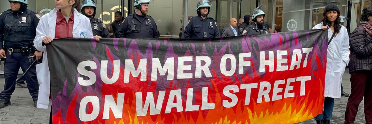 Climate protesters hold a banner reading "summer of heat on Wall Street" while cops stand behind them.