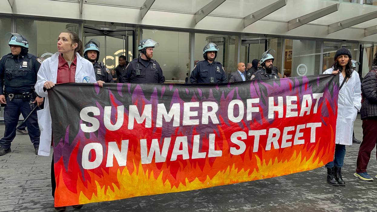 Climate protesters hold a banner reading "summer of heat on Wall Street" while cops stand behind them.