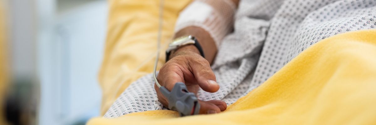 Close-up of a male patient's hand in a hospital bed with oximeter