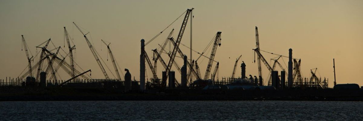 Construction cranes rise from the water against a sunset.