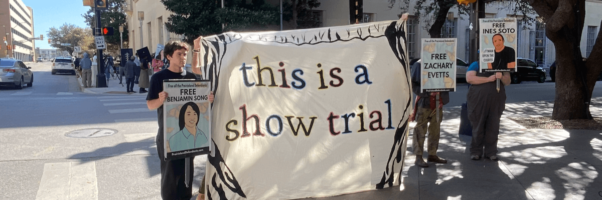 Demonstrators hold a banner reading "this is a show trial" outside court during the trial of Prairieview anti-ICE protesters