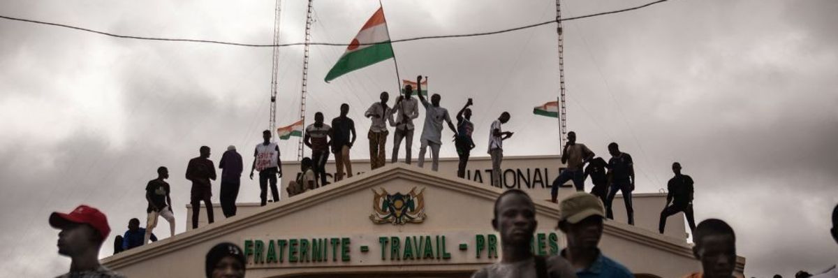 Demonstrators stand on top of a building with a Niger flag.