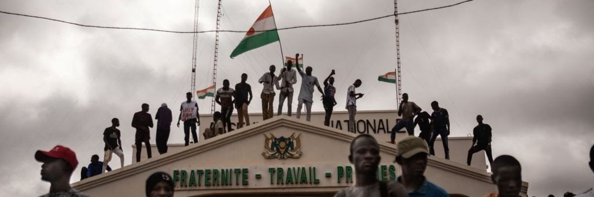 Demonstrators stand on top of a building with a Niger flag. 