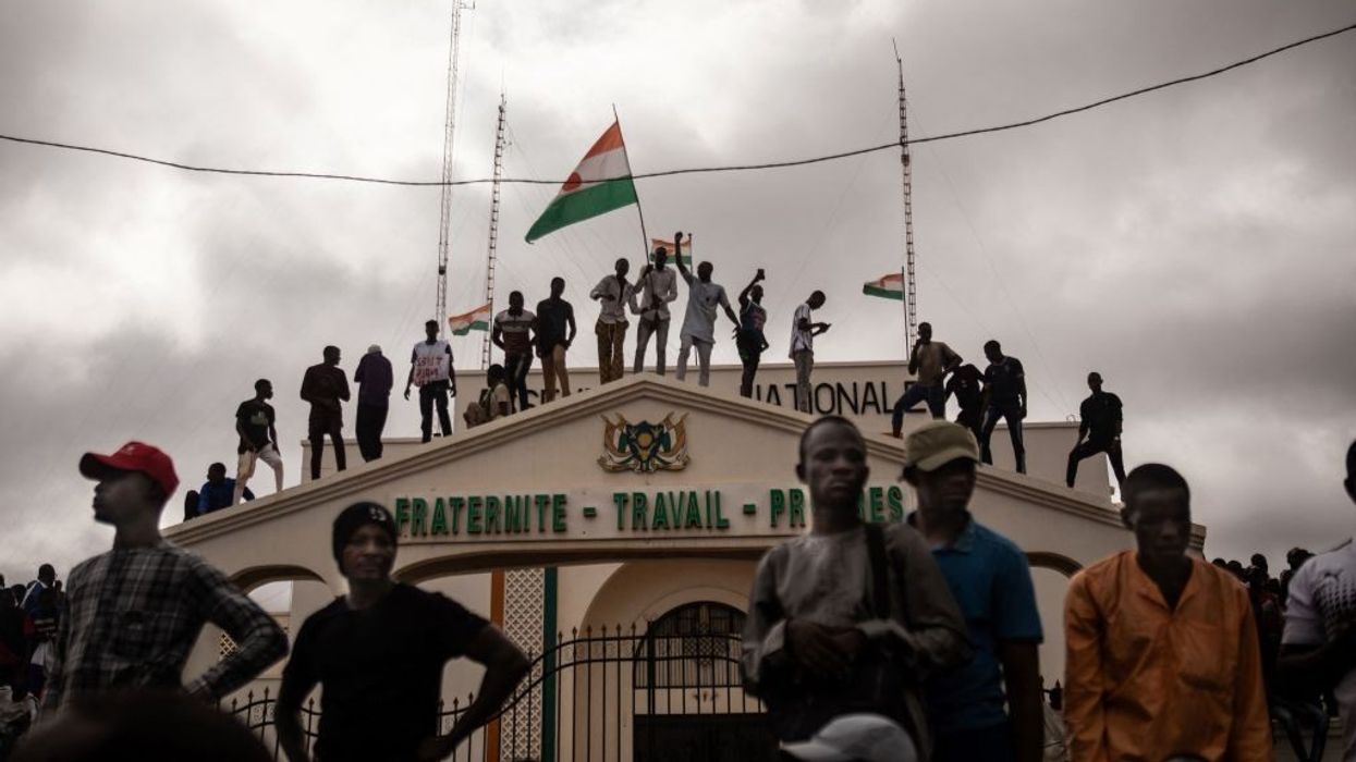 Demonstrators stand on top of a building with a Niger flag.
