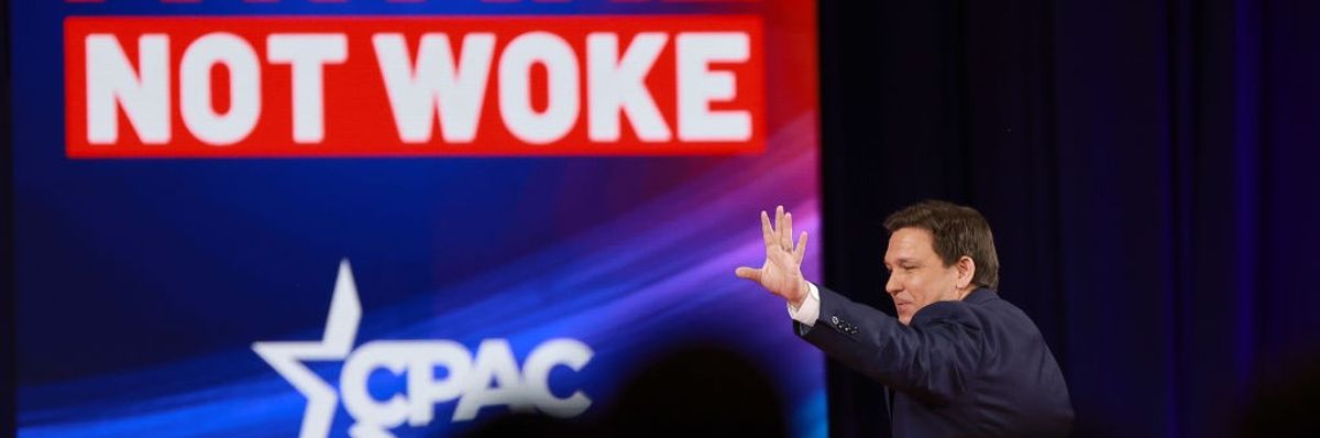 DeSantis waves to a CPAC audience under a videoscreen reading "Awake not woke"