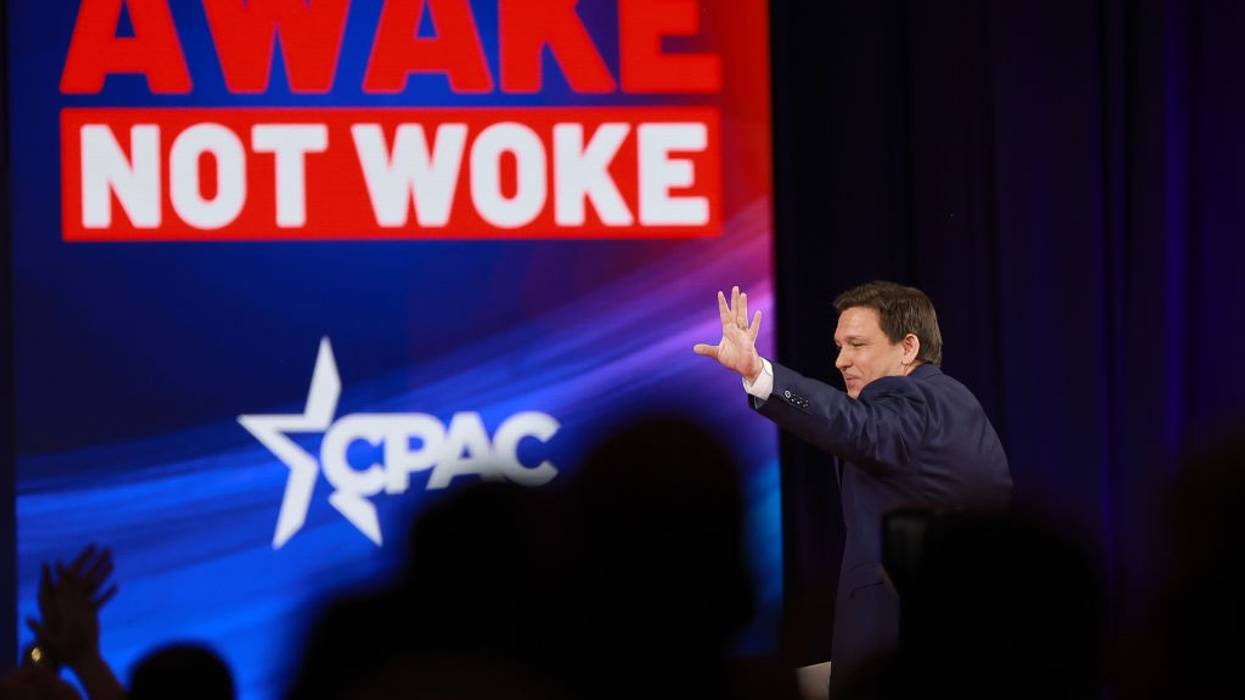 DeSantis waves to a CPAC audience under a videoscreen reading "Awake not woke"