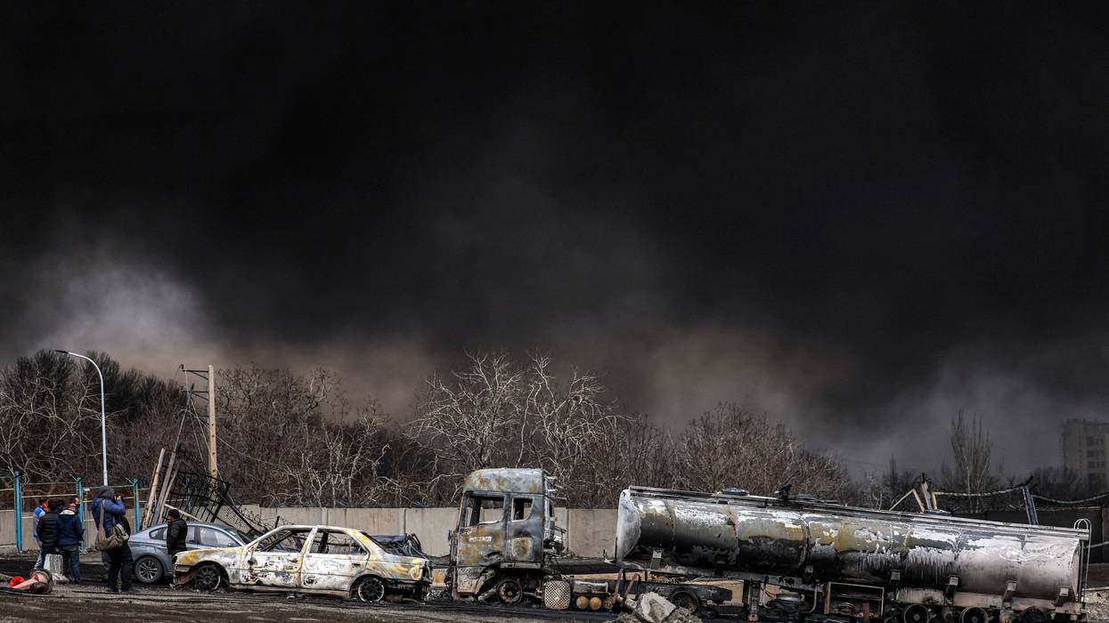 Destroyed vehicles in front of a dark cloud from US strikes on Iran.