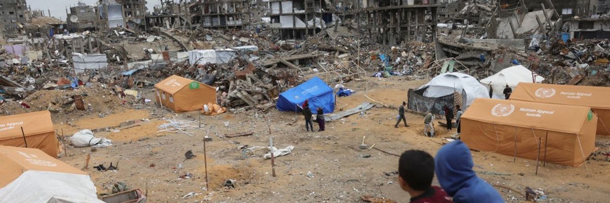 Displaced Palestinian children sit on a sand mound overlooking tents