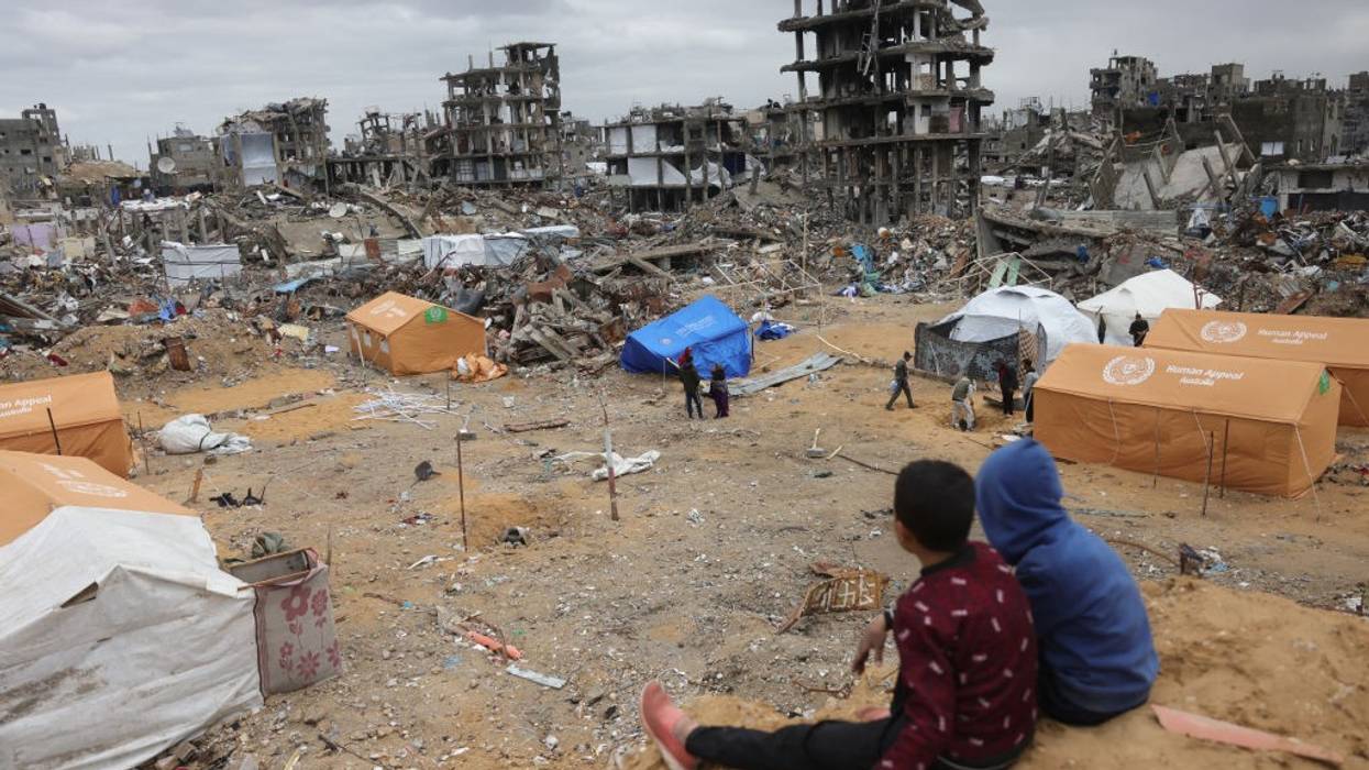 Displaced Palestinian children sit on a sand mound overlooking tents