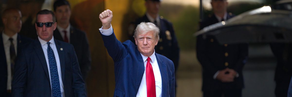 Donald Trump leaves Trump Tower wearing blue suit, white shirt, and red tie, with his fist raised in the air