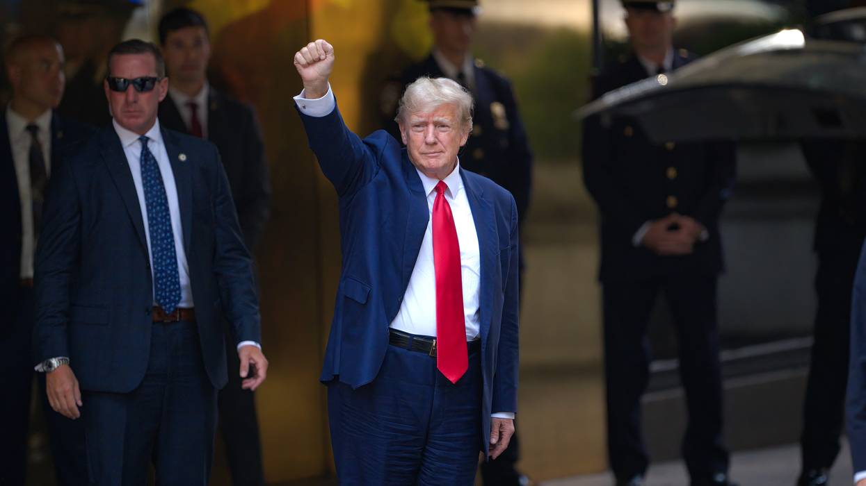 Donald Trump leaves Trump Tower wearing blue suit, white shirt, and red tie, with his fist raised in the air