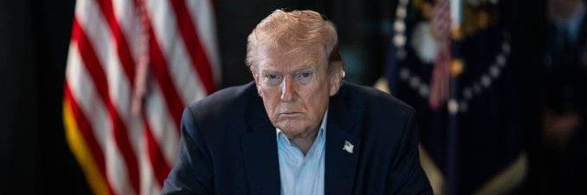 Donald Trump sittting at a desk with flags behind him