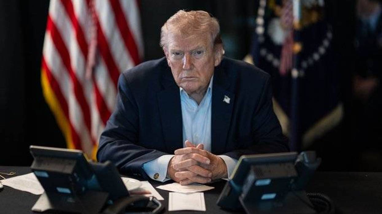 Donald Trump sittting at a desk with flags behind him