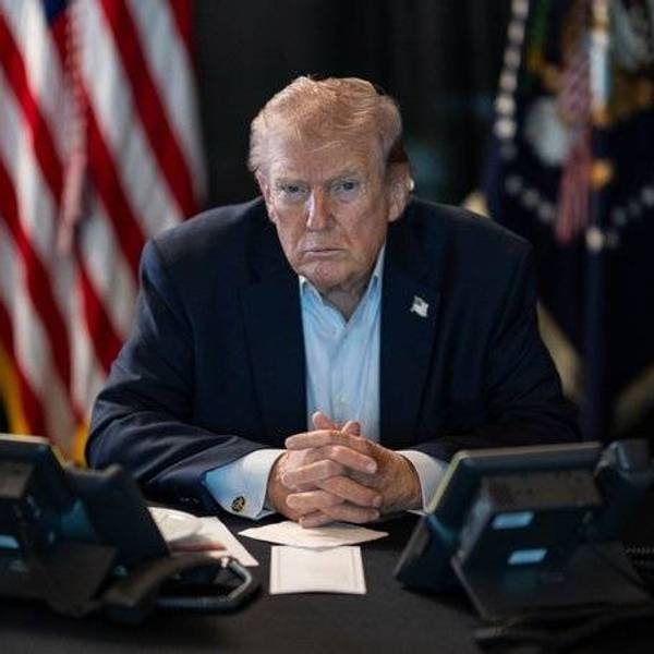 Donald Trump sittting at a desk with flags behind him