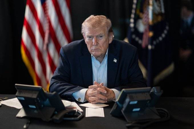 Donald Trump sittting at a desk with flags behind him