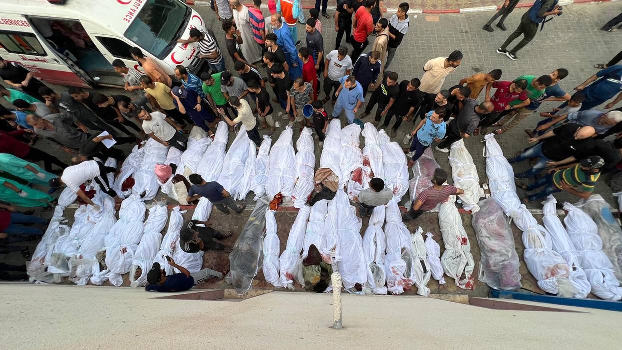 Dozens of dead Palestinians are wrapped in shrounds, some bloody