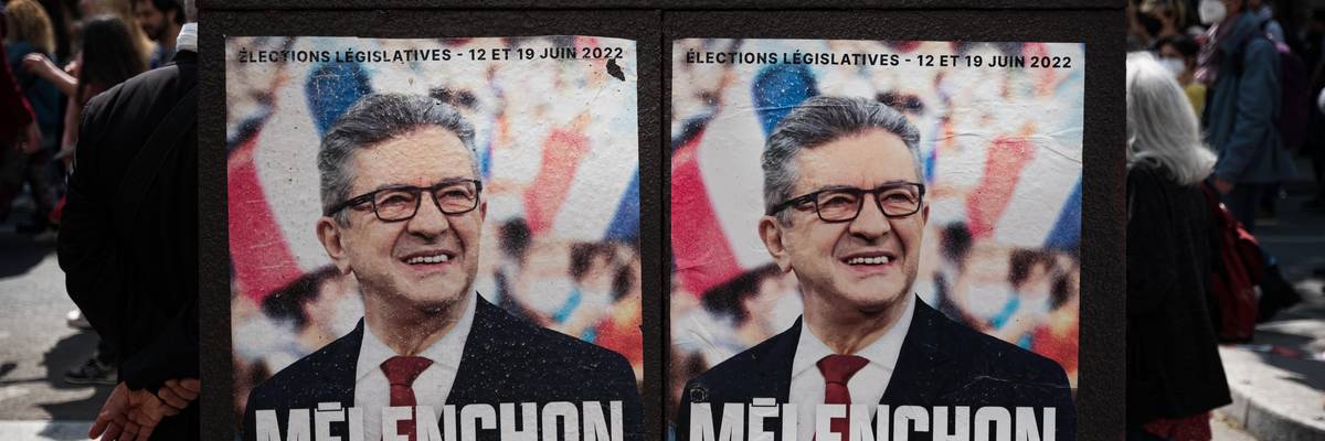 During a May Day demonstration in Paris, people walk past campaign posters for the June 2022 legislative election that portray left-wing MP Jean-Luc Mélenchon as prime minister.