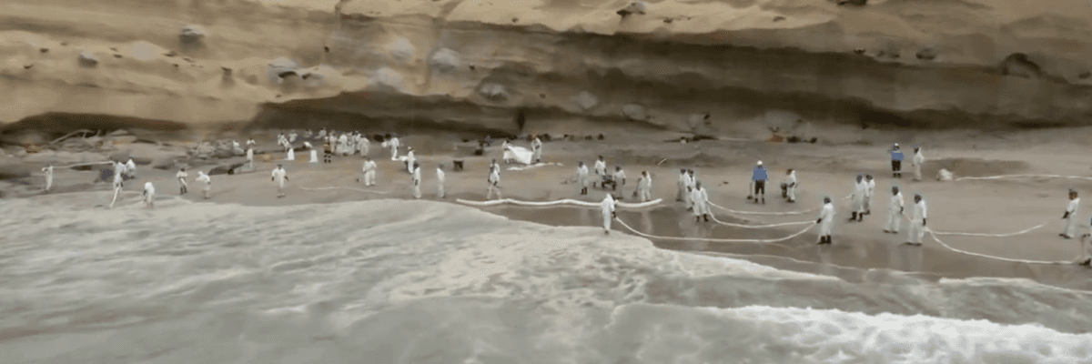 Emergency workers try to contain an oil spill on a beach in Peru